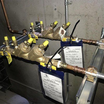 Deux clapets anti-retour d'eau en bronze avec étiquettes et tuyaux en cuivre, montés sur un mur en béton.