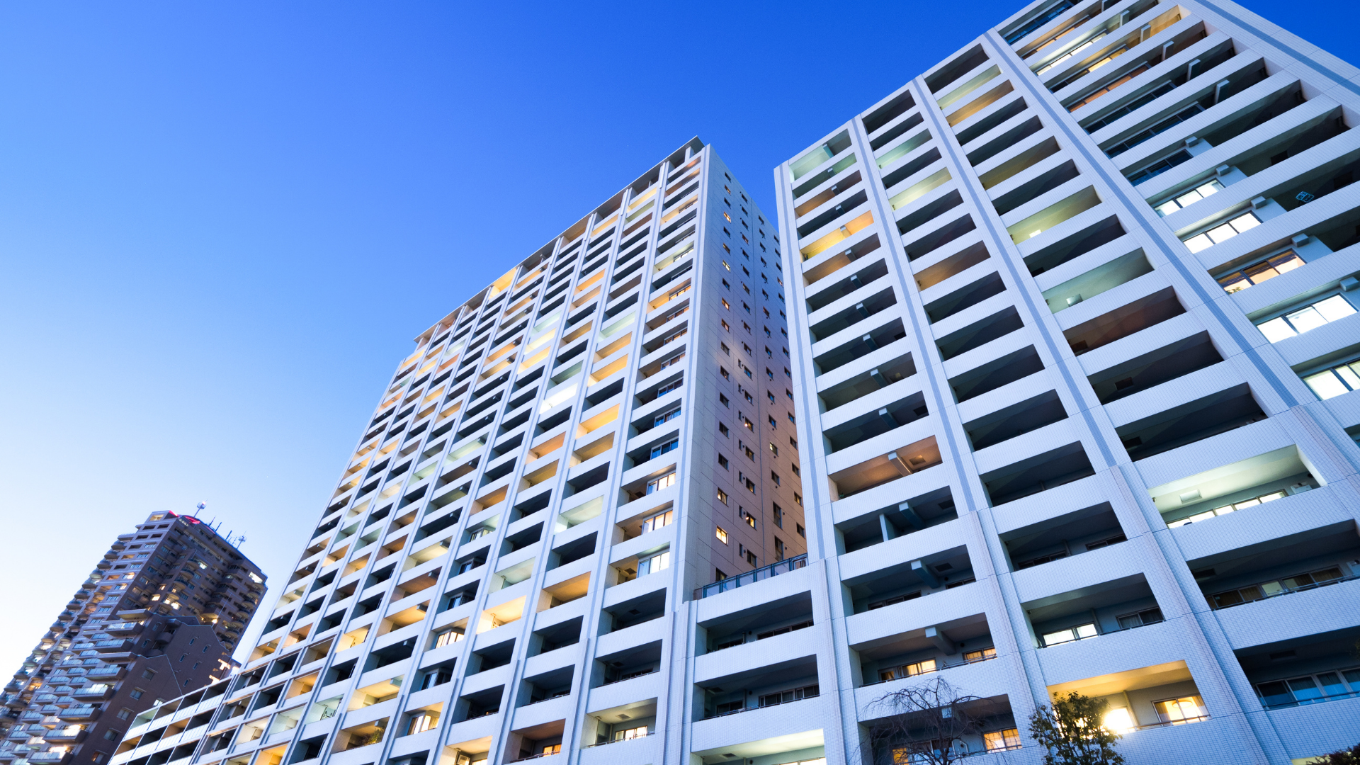 Low-angle view of two modern white high-rise apartment buildings against a clear blue evening sky.
