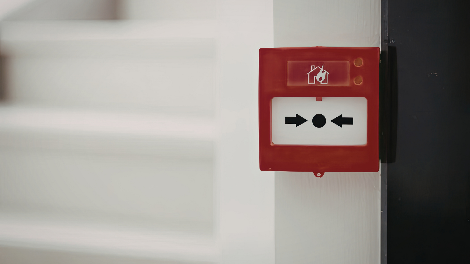 A red fire alarm manual call point mounted on a white wall.