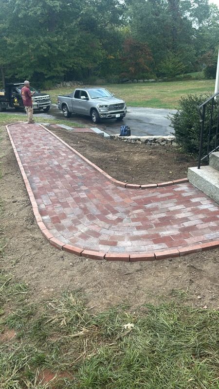 Brick walkway curves to house entrance; a person stands by a truck on the driveway.