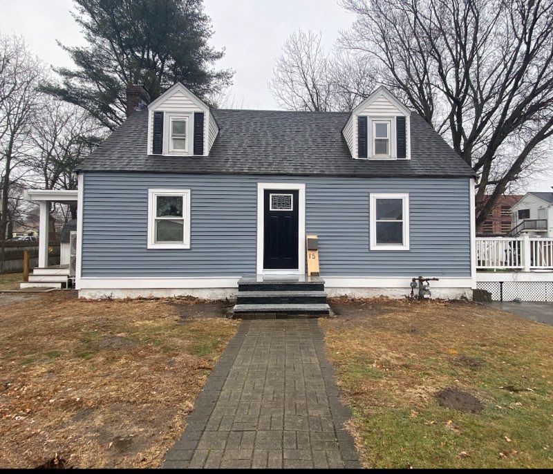 Blue-sided house with black door, two dormers, and a brick path. Overcast day.