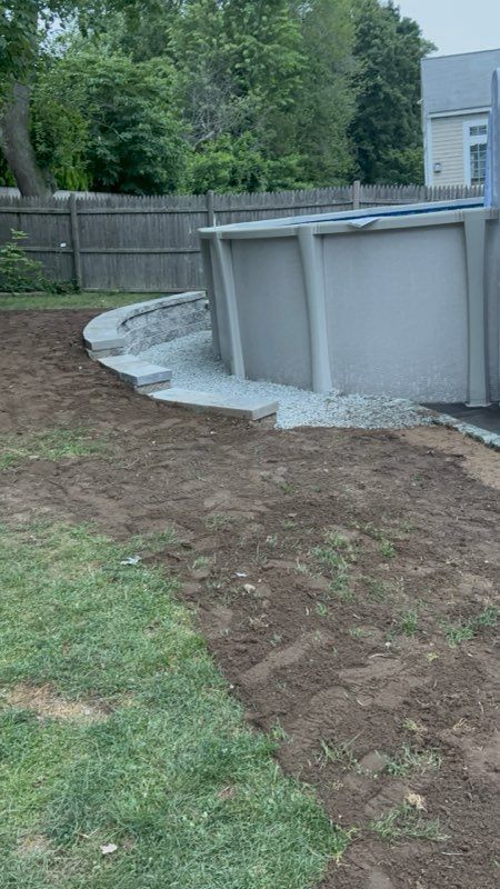 Backyard with an above-ground pool, gravel steps, and a dirt path near a lawn.