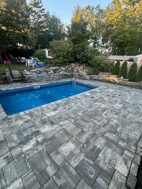 Backyard pool with stone patio, trees, and lush greenery.