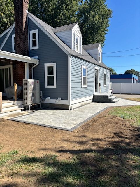 Blue house with gray patio. Yard has fresh dirt. Sunny day.