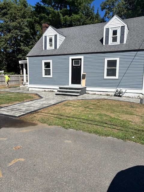 A blue house with a new stone walkway and steps; person in the yard working on the walkway.