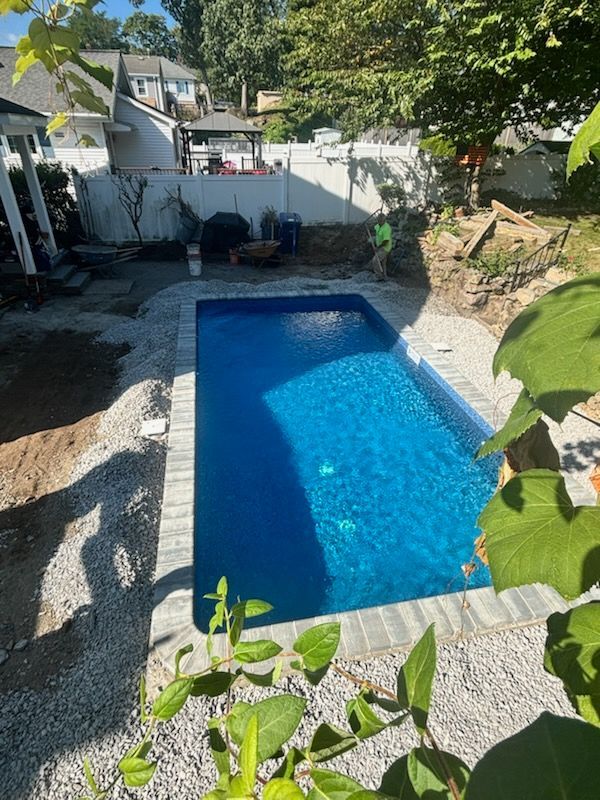 Rectangular blue pool in a backyard surrounded by light-colored gravel and paving stones.