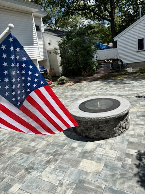American flag waves near a stone fire pit on a paved patio.
