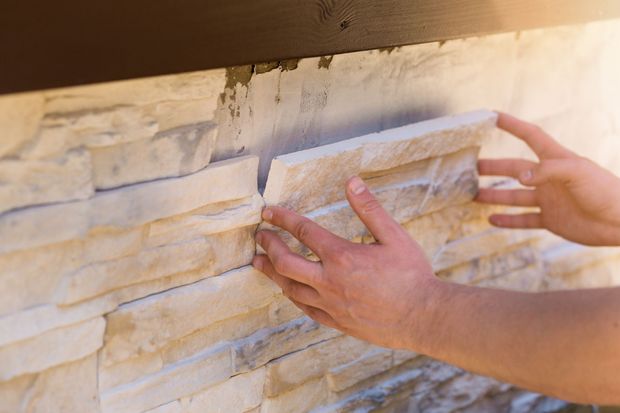 Hands placing a stone veneer tile on a wall.
