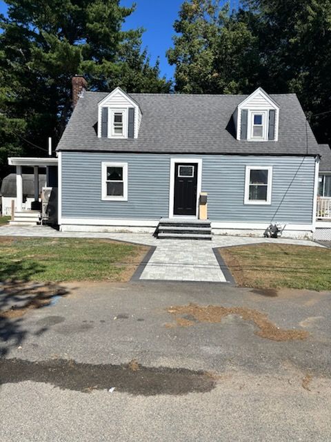 Gray house with black door, white trim, and walkway; blue siding, green grass, clear sky.