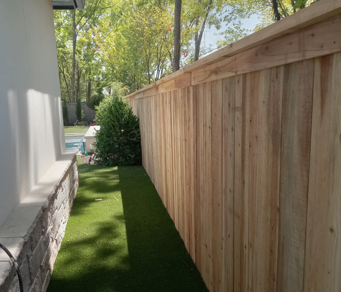A wooden fence surrounds a lush green lawn in a backyard.
