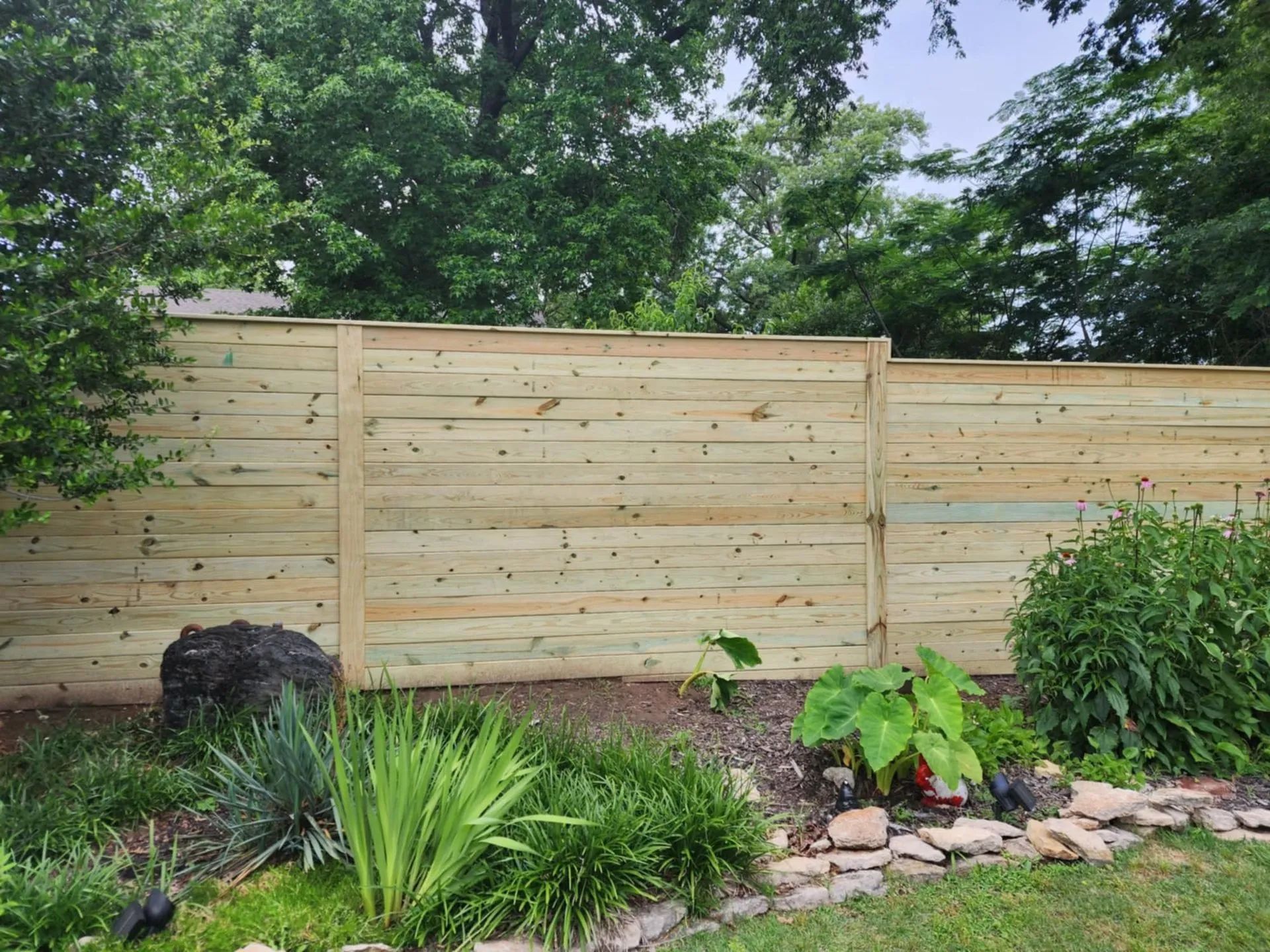 Wooden horizontal plank fence in a backyard garden.