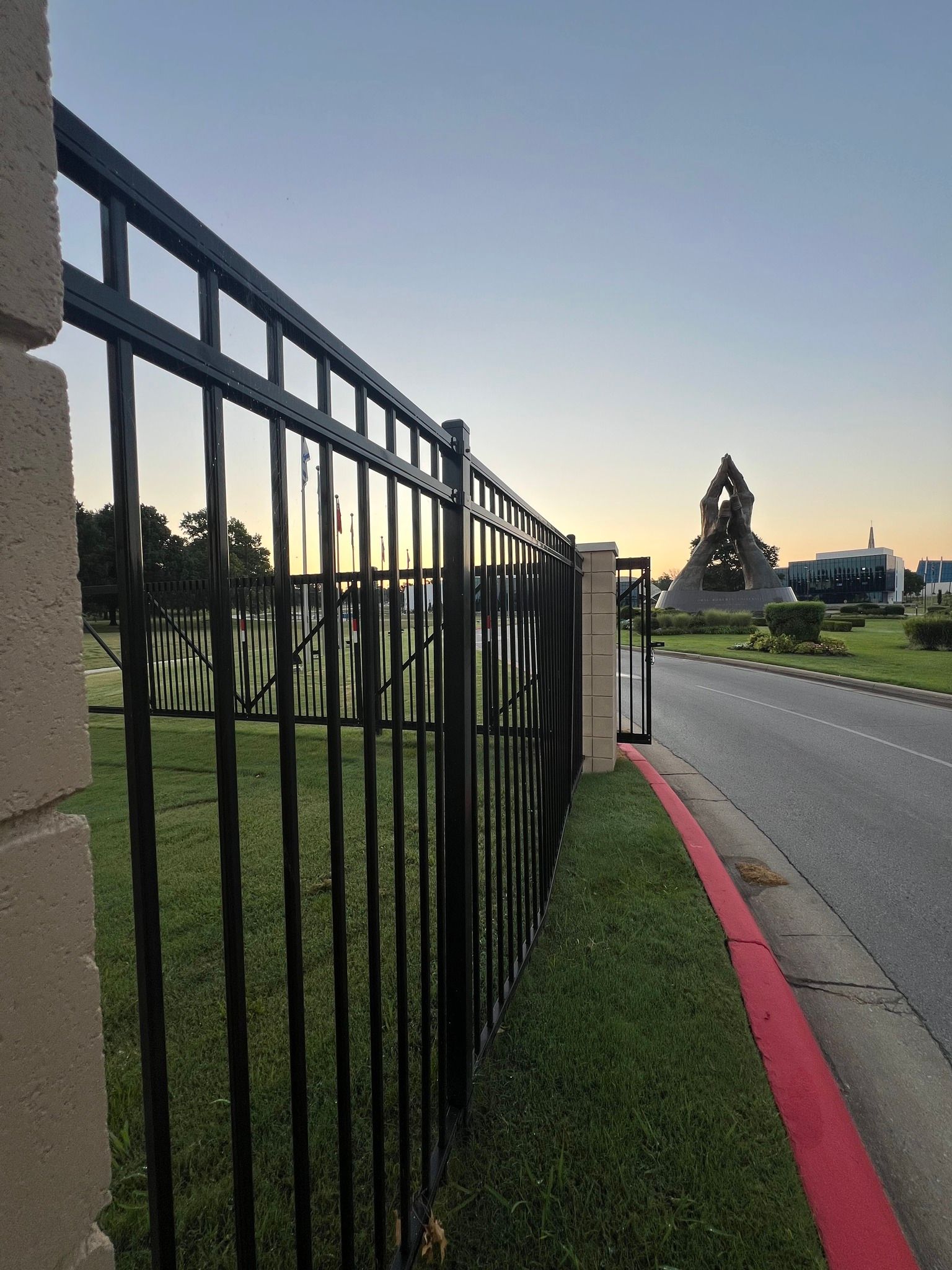 A black metal fence surrounds a grassy area next to a road.