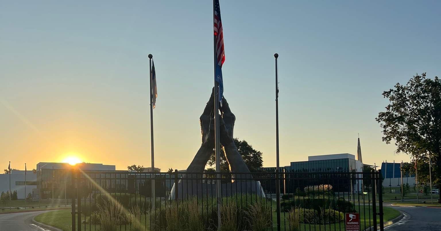The sun is setting behind a statue of a man holding an american flag.