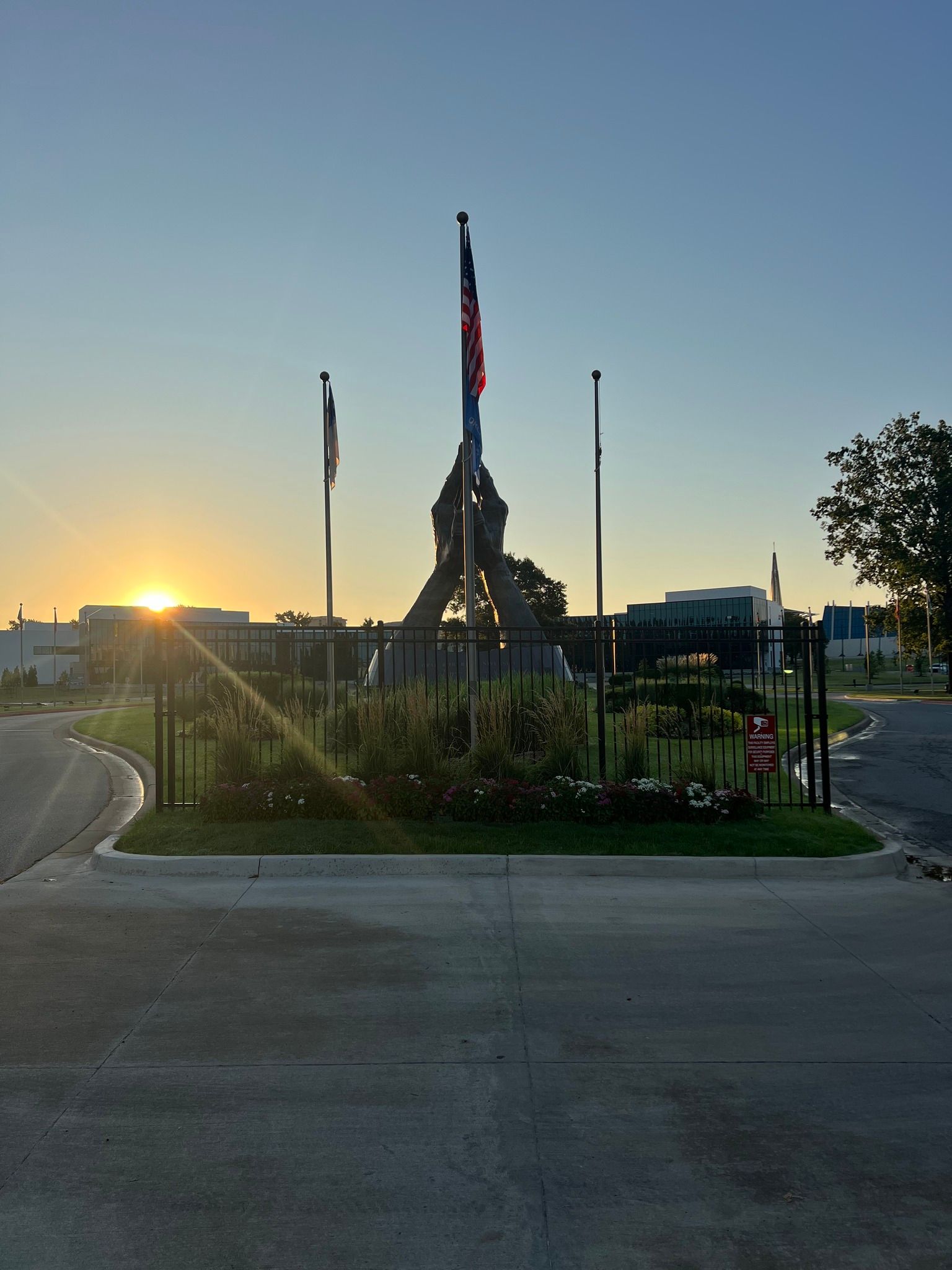 The sun is setting behind a statue in a park