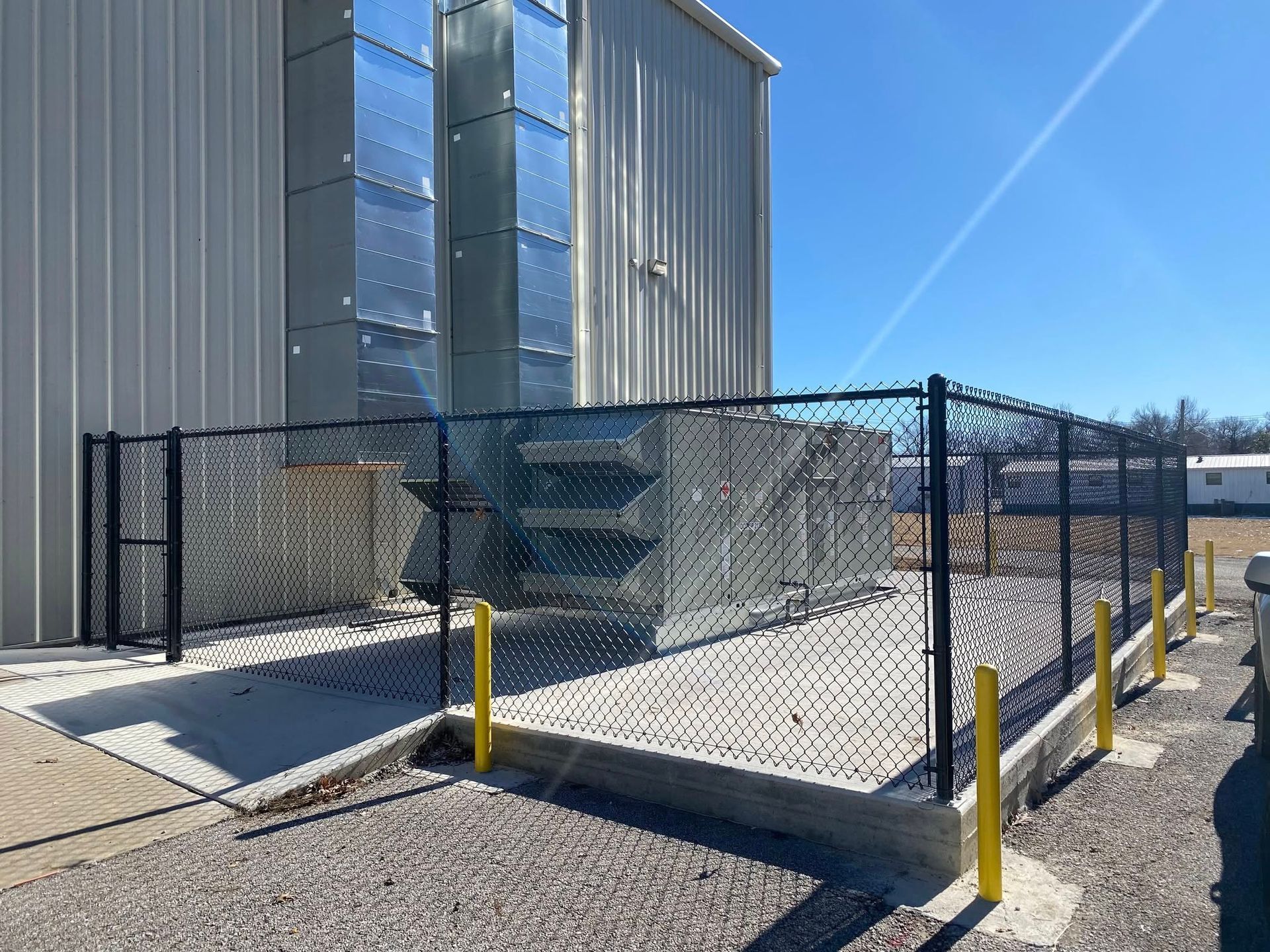 A chain link fence surrounds a building with a ventilation system behind it.