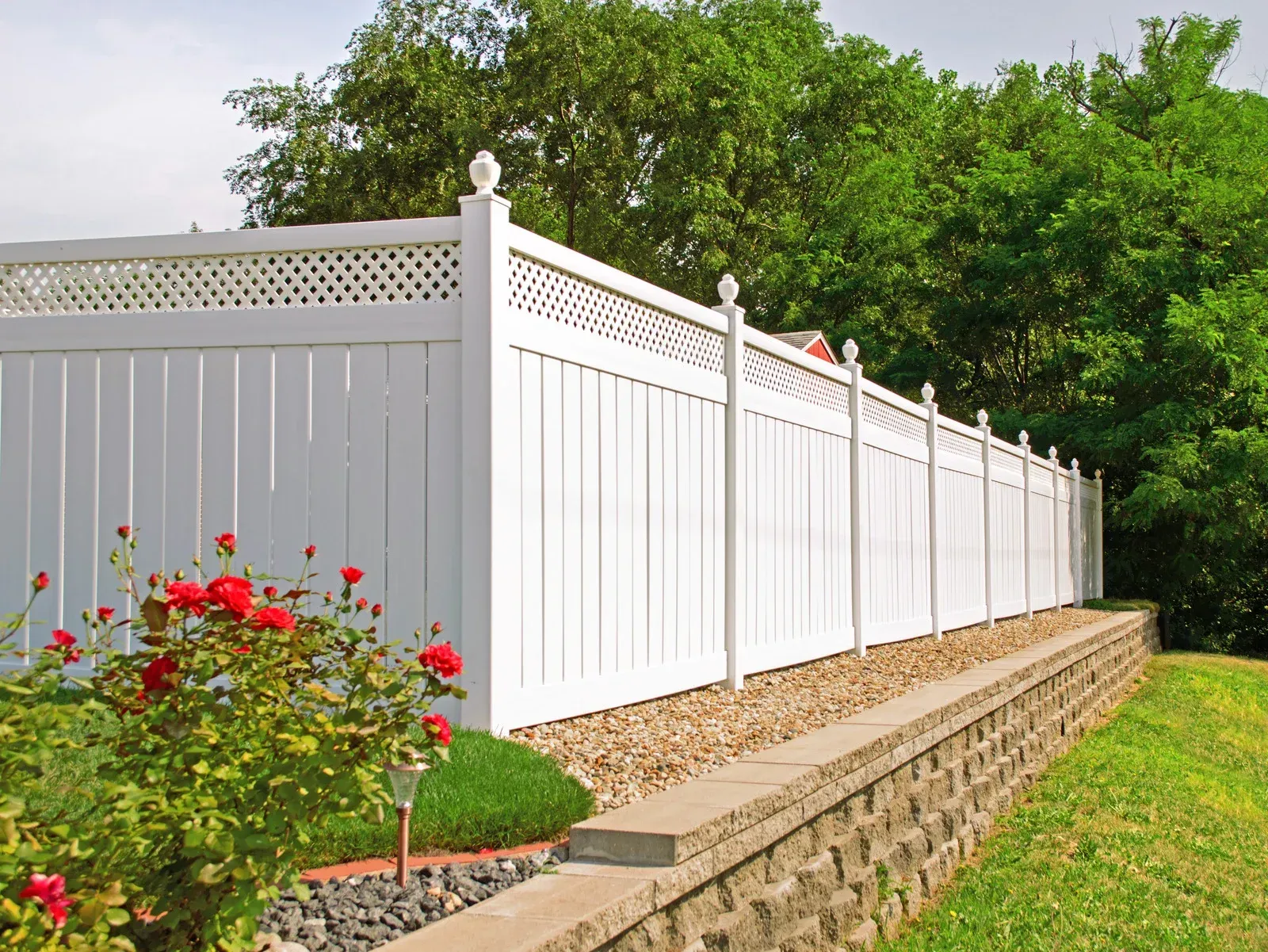 A white fence surrounds a stone wall in a yard