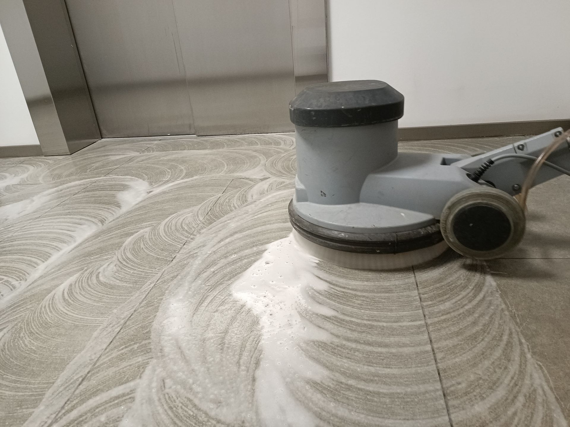 A machine is cleaning a tiled floor in a building.