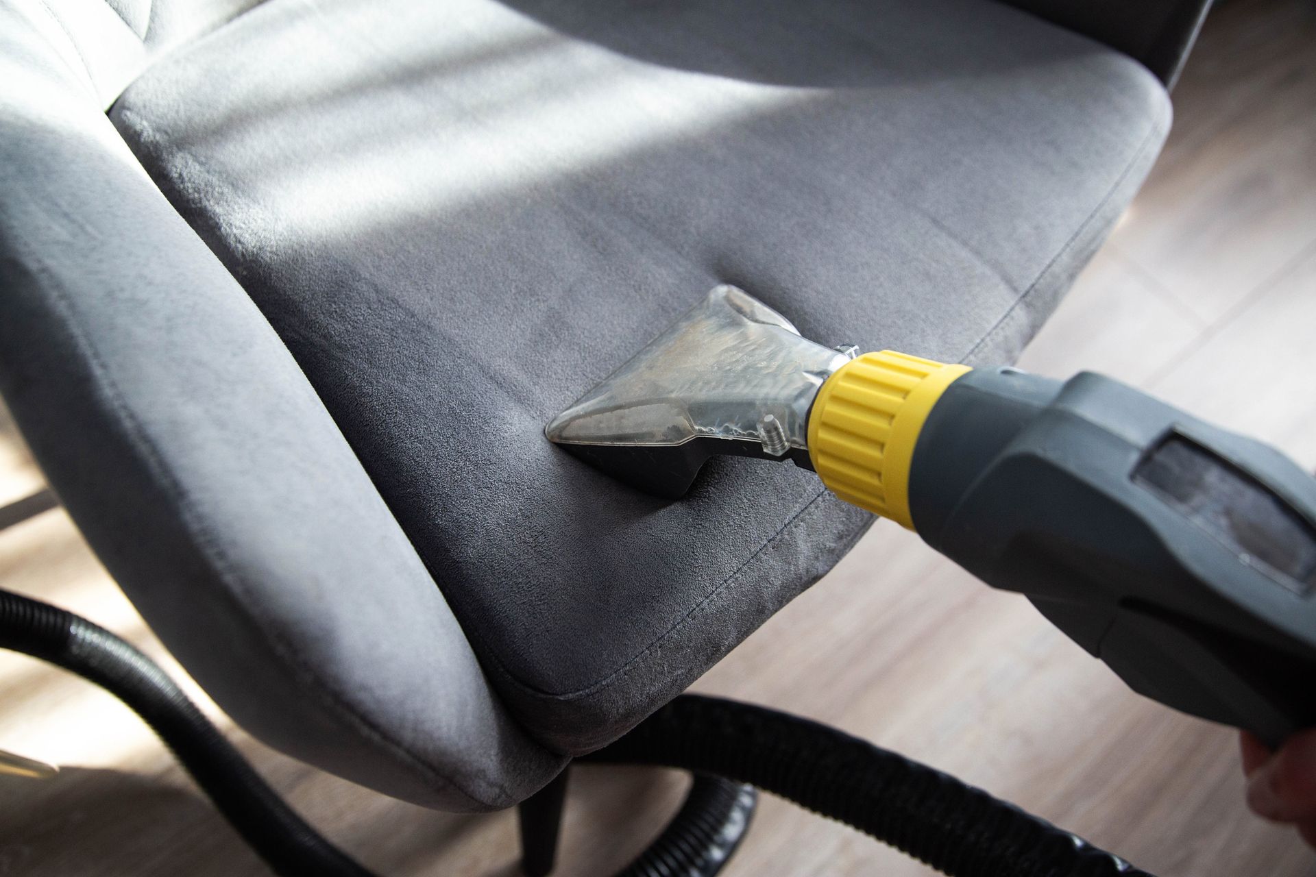 A person is cleaning a chair with a vacuum cleaner.