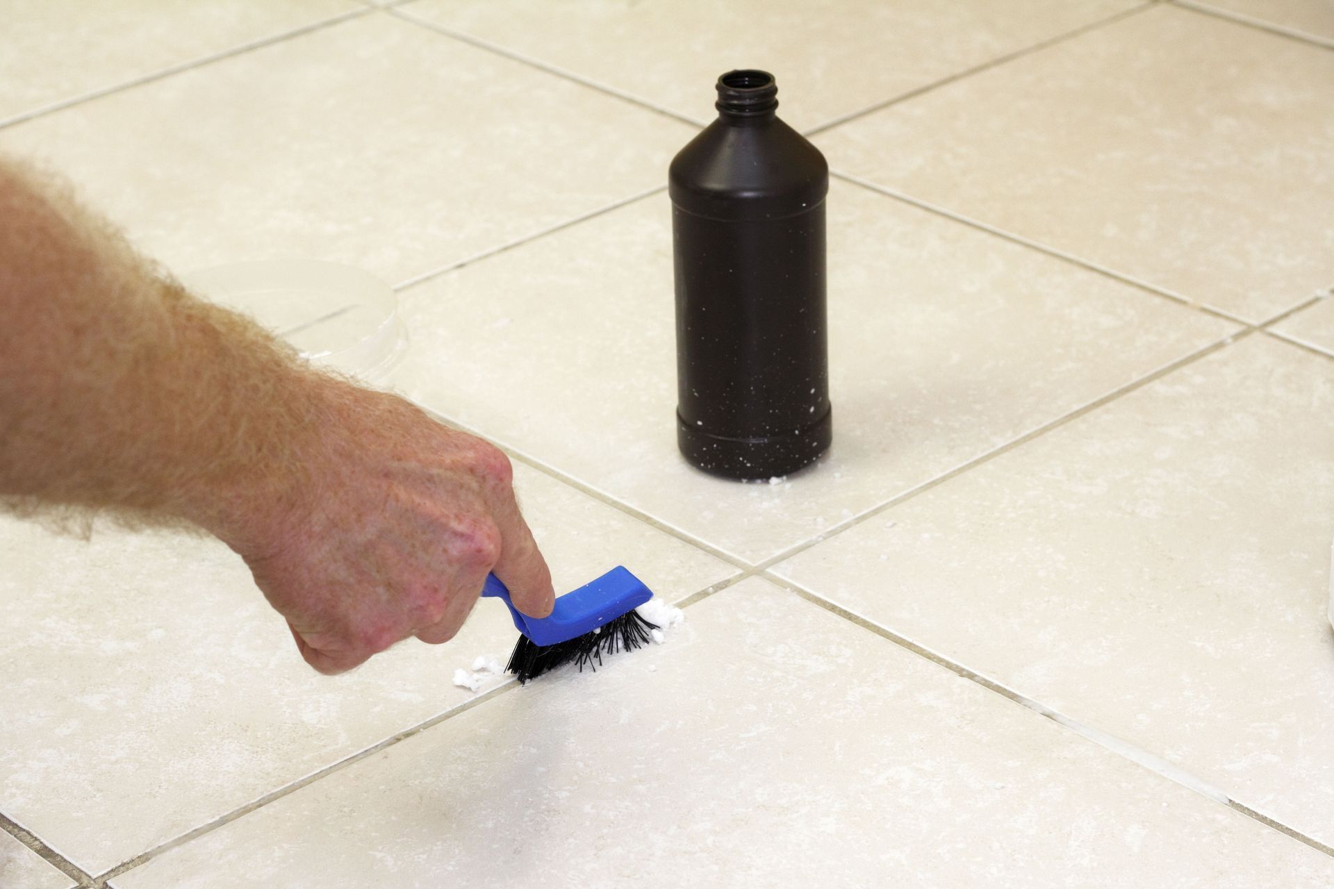 A person is cleaning a tile floor with a blue brush.