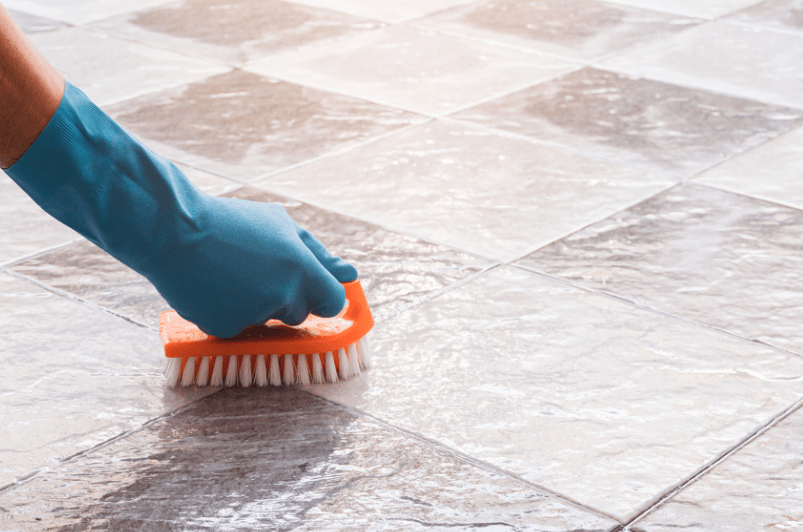 A person is cleaning a tile floor with a brush.