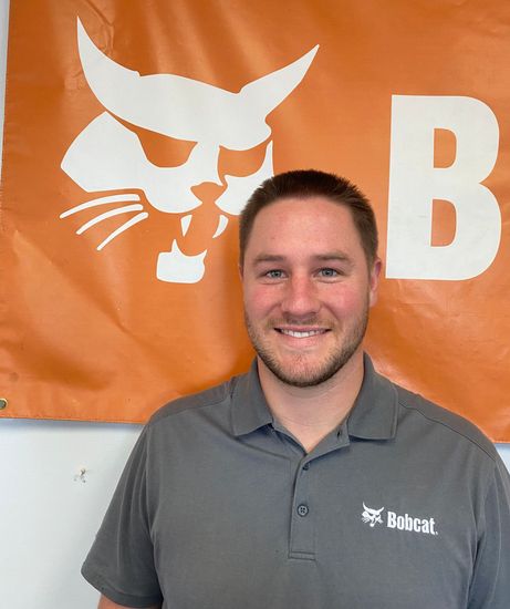 A man is standing in front of a bobcat banner.