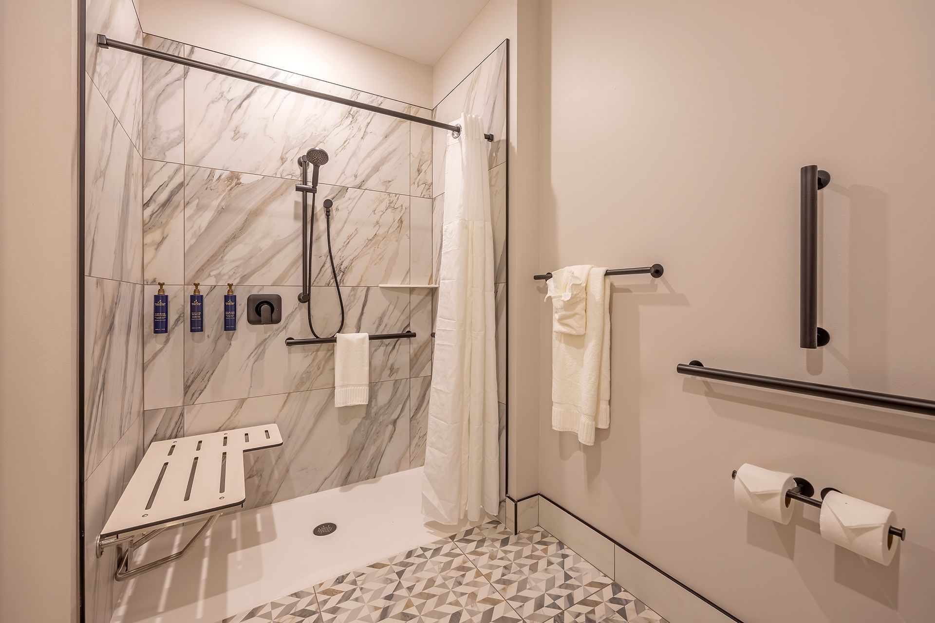 Accessible bathroom with roll-in shower, grab bars, and fold-down seat.