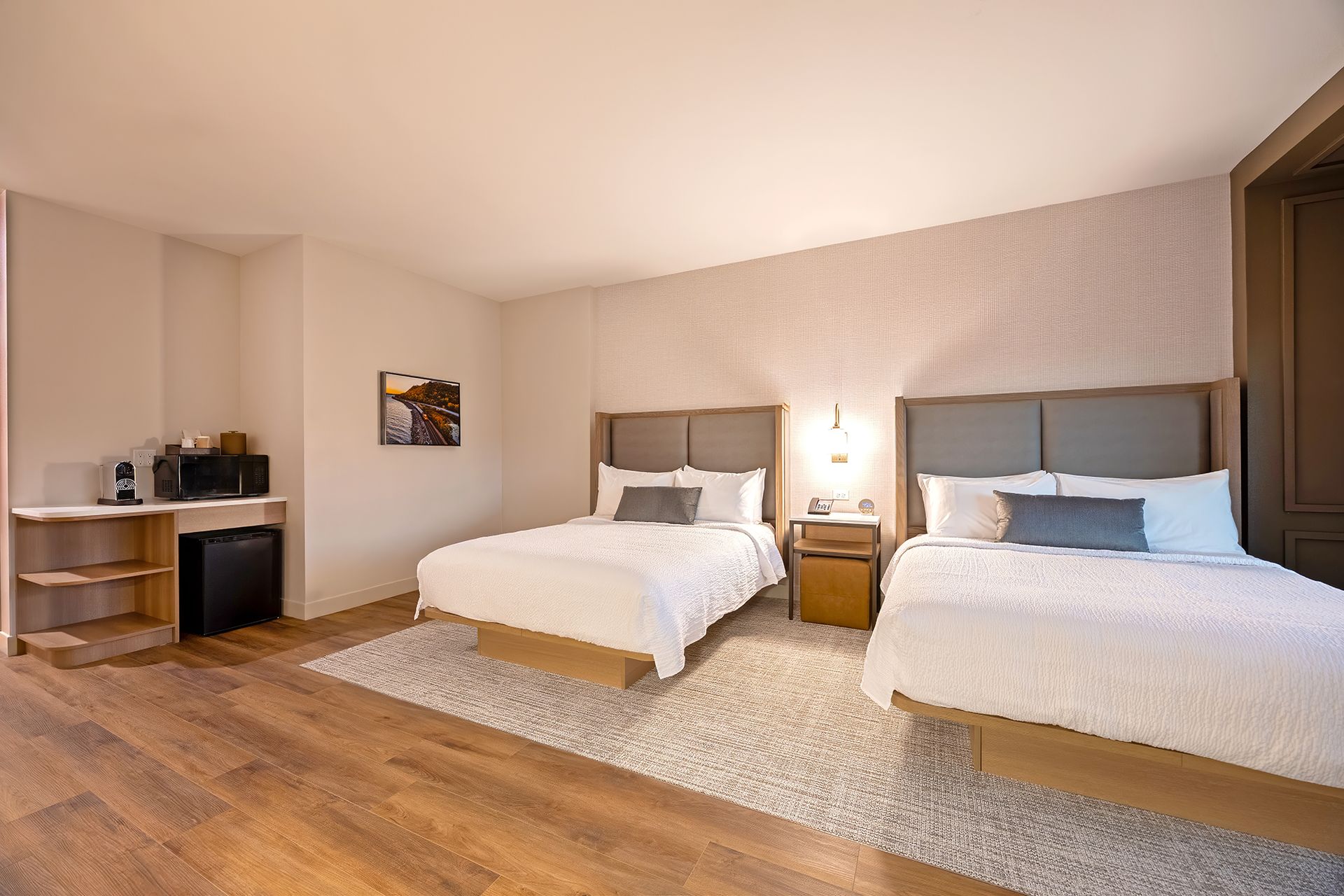 Hotel room with two beds, a rug, microwave, and small table. Wooden floor and neutral colored walls.