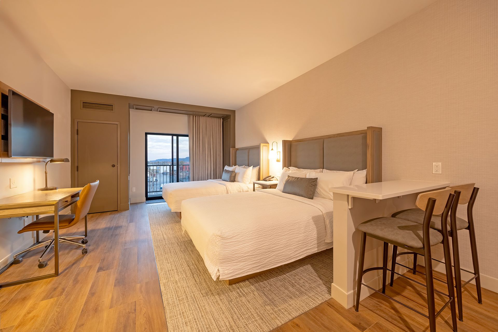 Hotel room with two beds, desk, balcony, and small counter with bar stools.