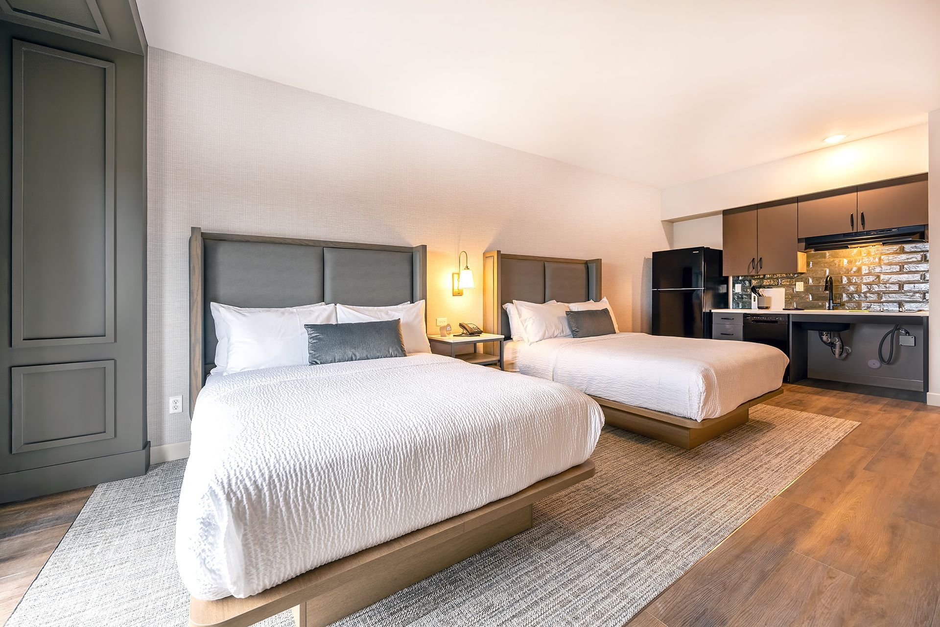 Hotel room with two beds, small kitchenette, wooden floors, and a carpet.