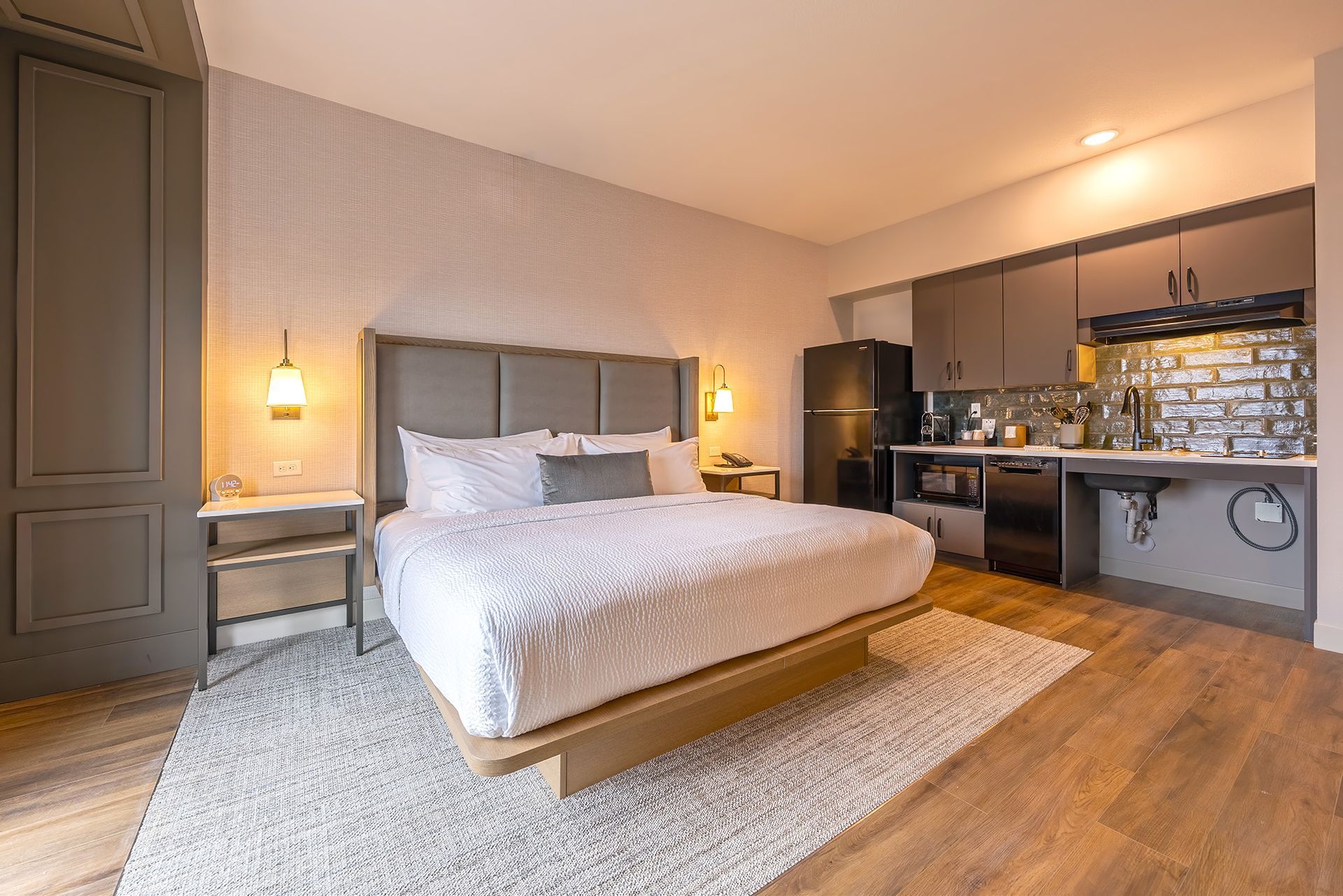 Hotel room with king bed, kitchenette, and neutral color scheme.