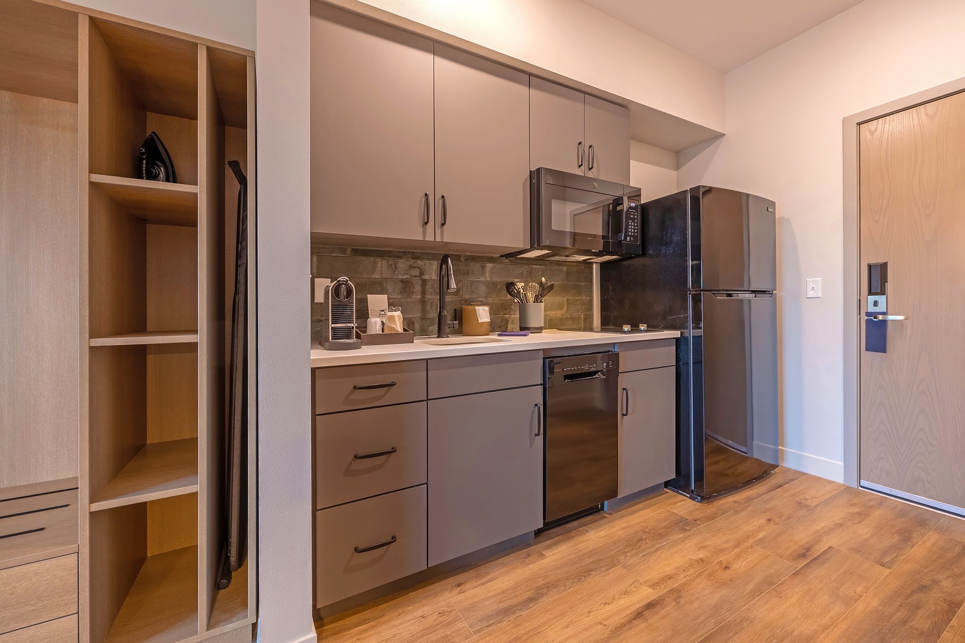 Studio apartment kitchen with cabinets, appliances, and wardrobe; wooden floors.