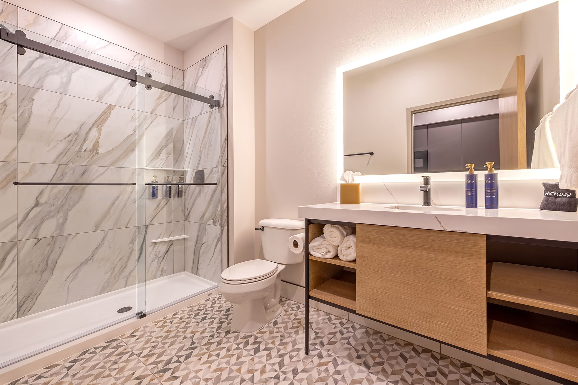 Modern bathroom with marble shower, patterned floor, and wooden vanity.
