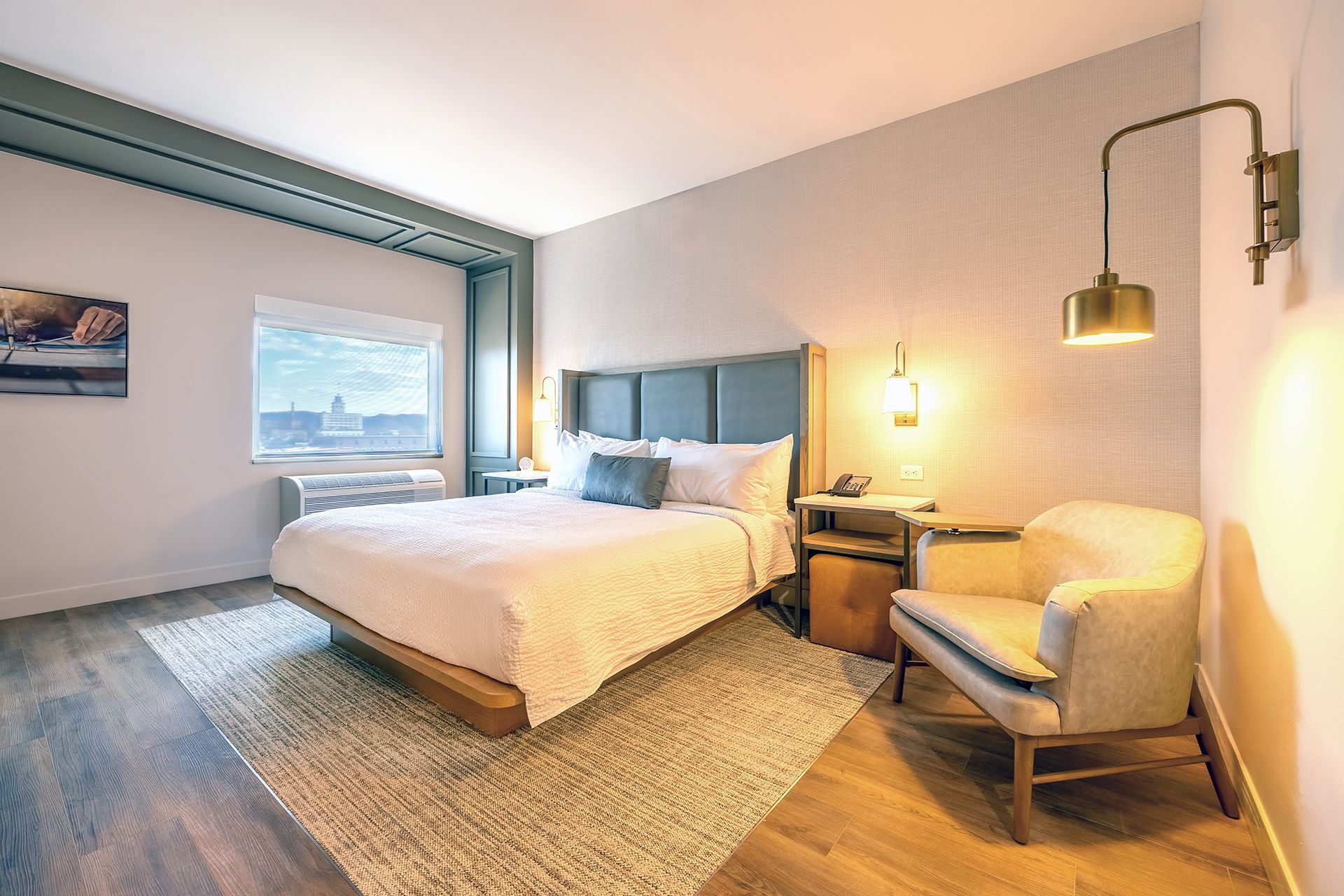 Hotel room with bed, chair, and side table; neutral tones, window view.