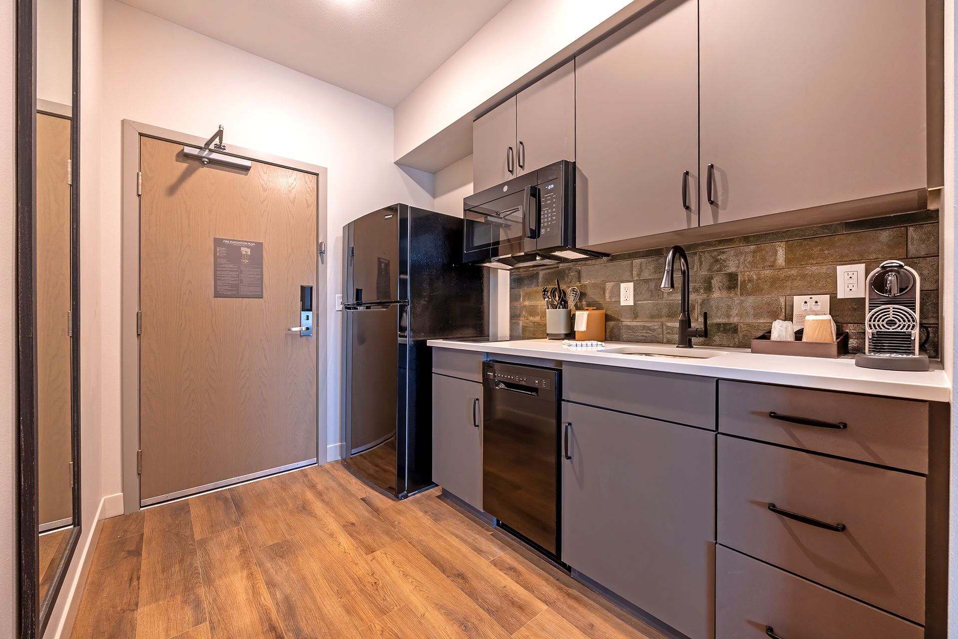 Small modern kitchen with grey cabinets, black appliances, and wood-look flooring.