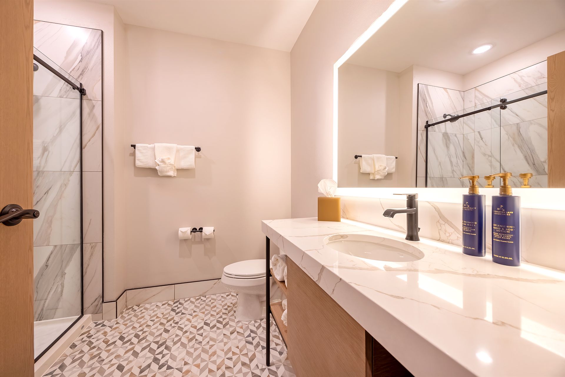 Modern bathroom with marble countertop, glass shower, and mosaic tile floor.