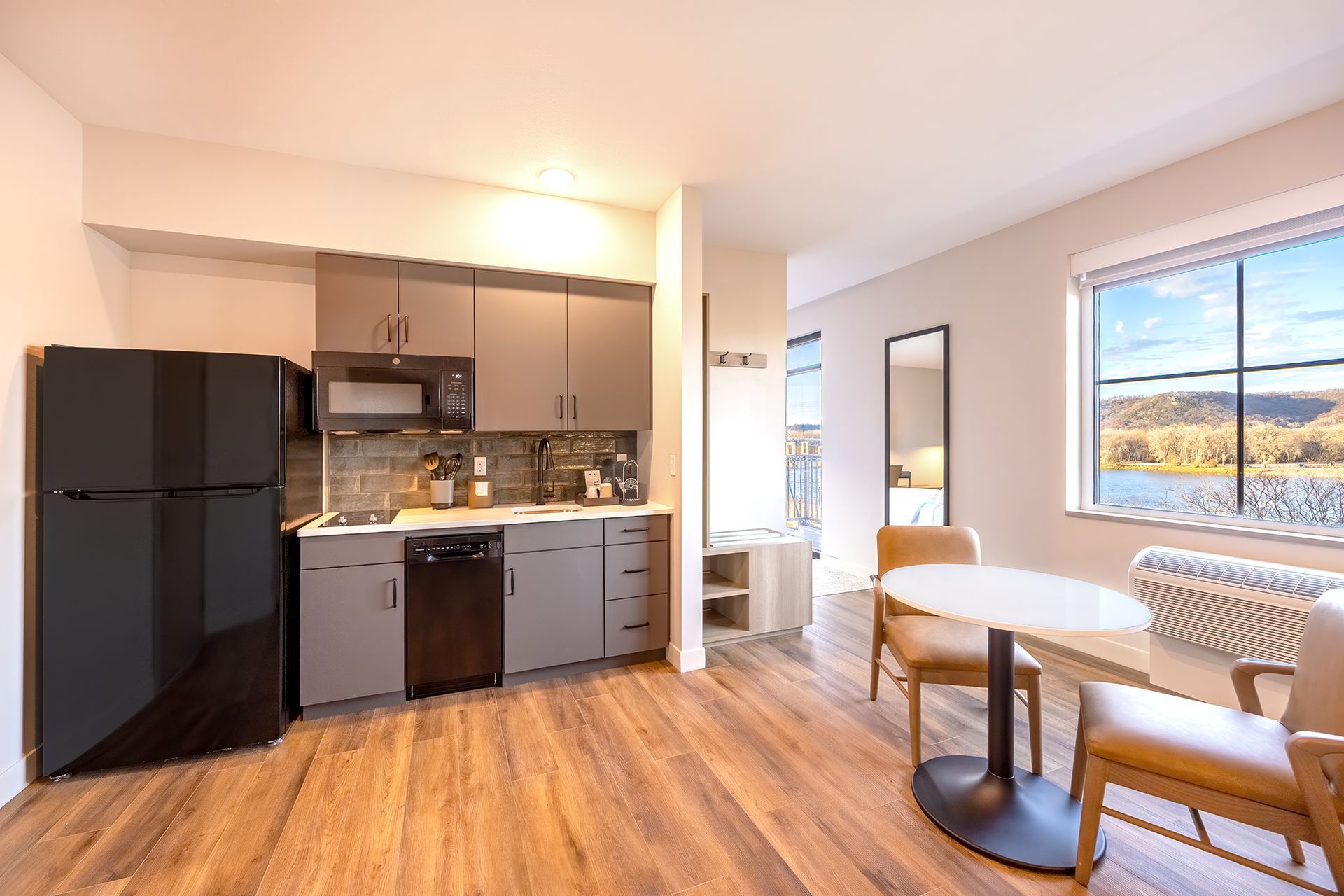 Modern studio kitchen with black appliances, gray cabinets, a small dining table, and large window with river view.
