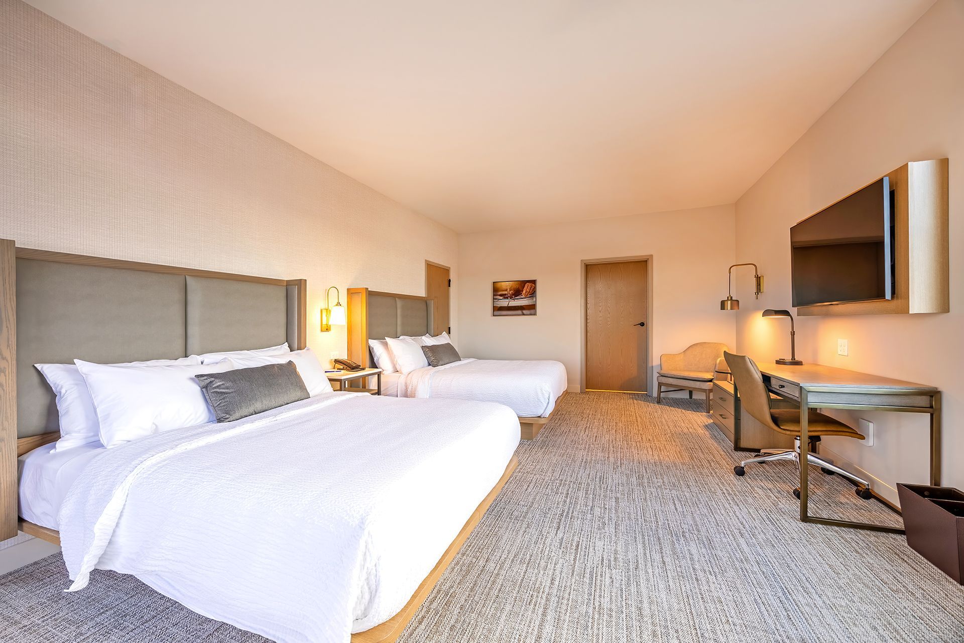 Hotel room with two queen beds, desk, TV, and neutral color scheme.