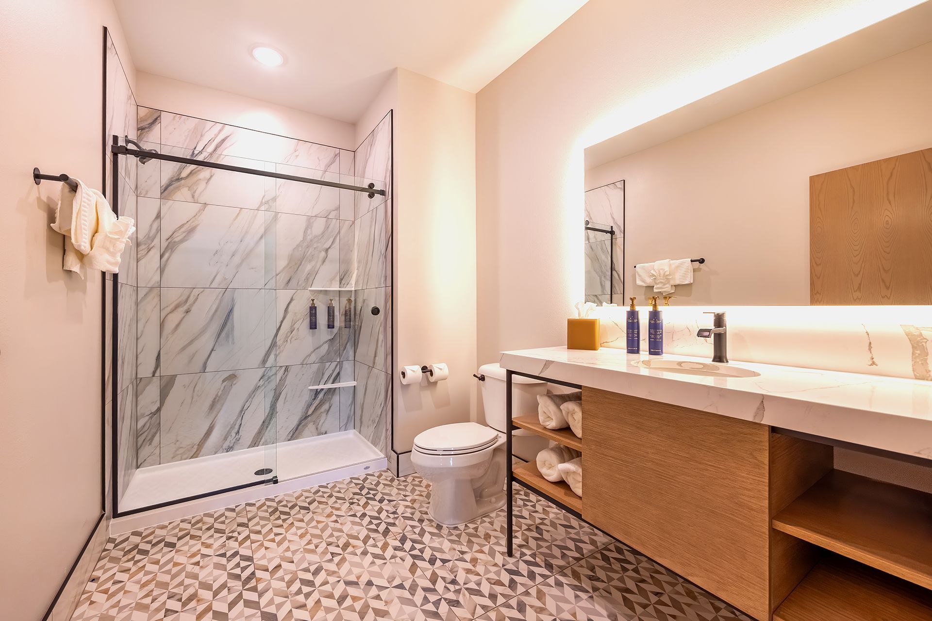 Modern bathroom with marble shower, vanity with large mirror, and patterned floor.