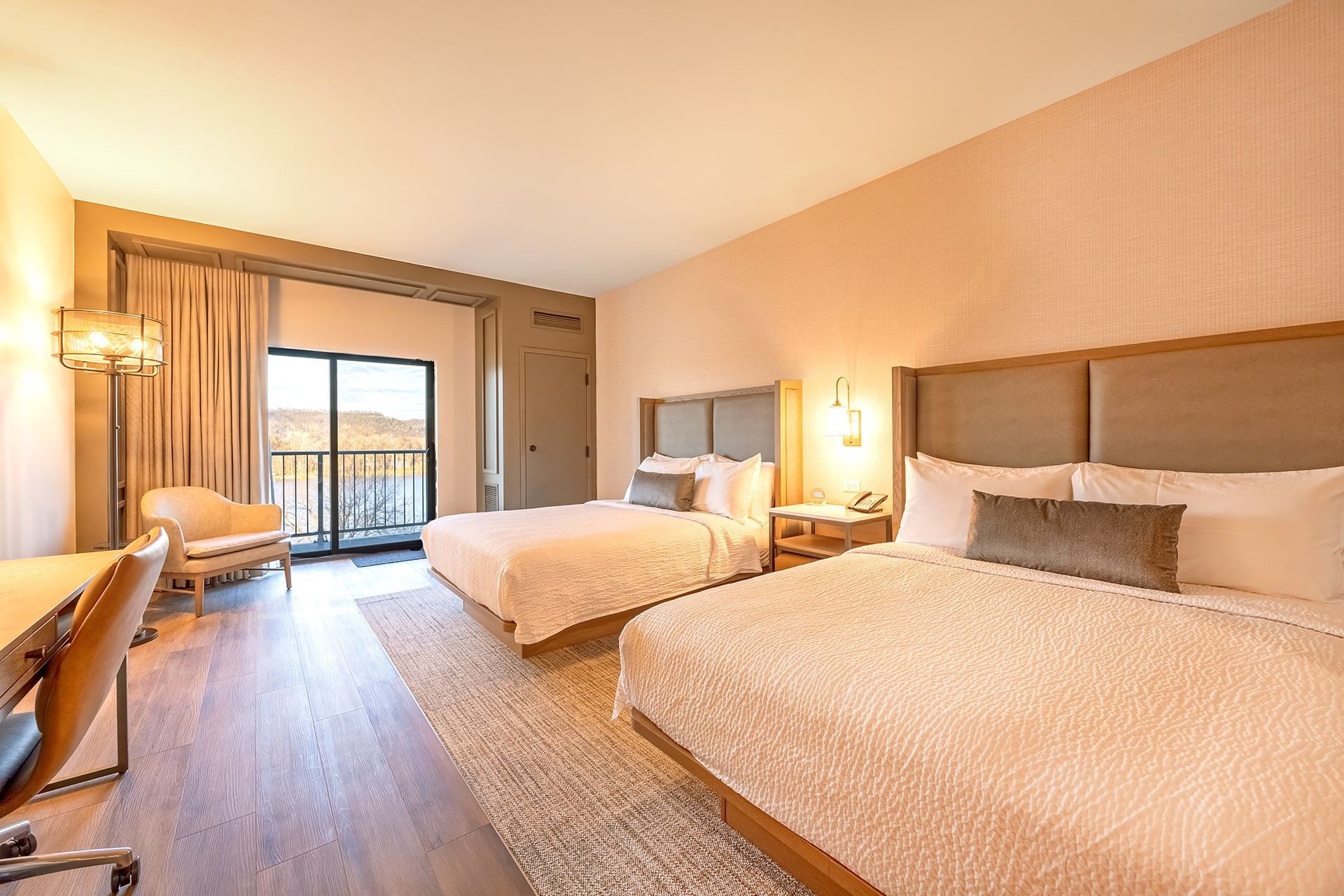 Hotel room with two queen beds, a balcony, desk, and neutral tones.