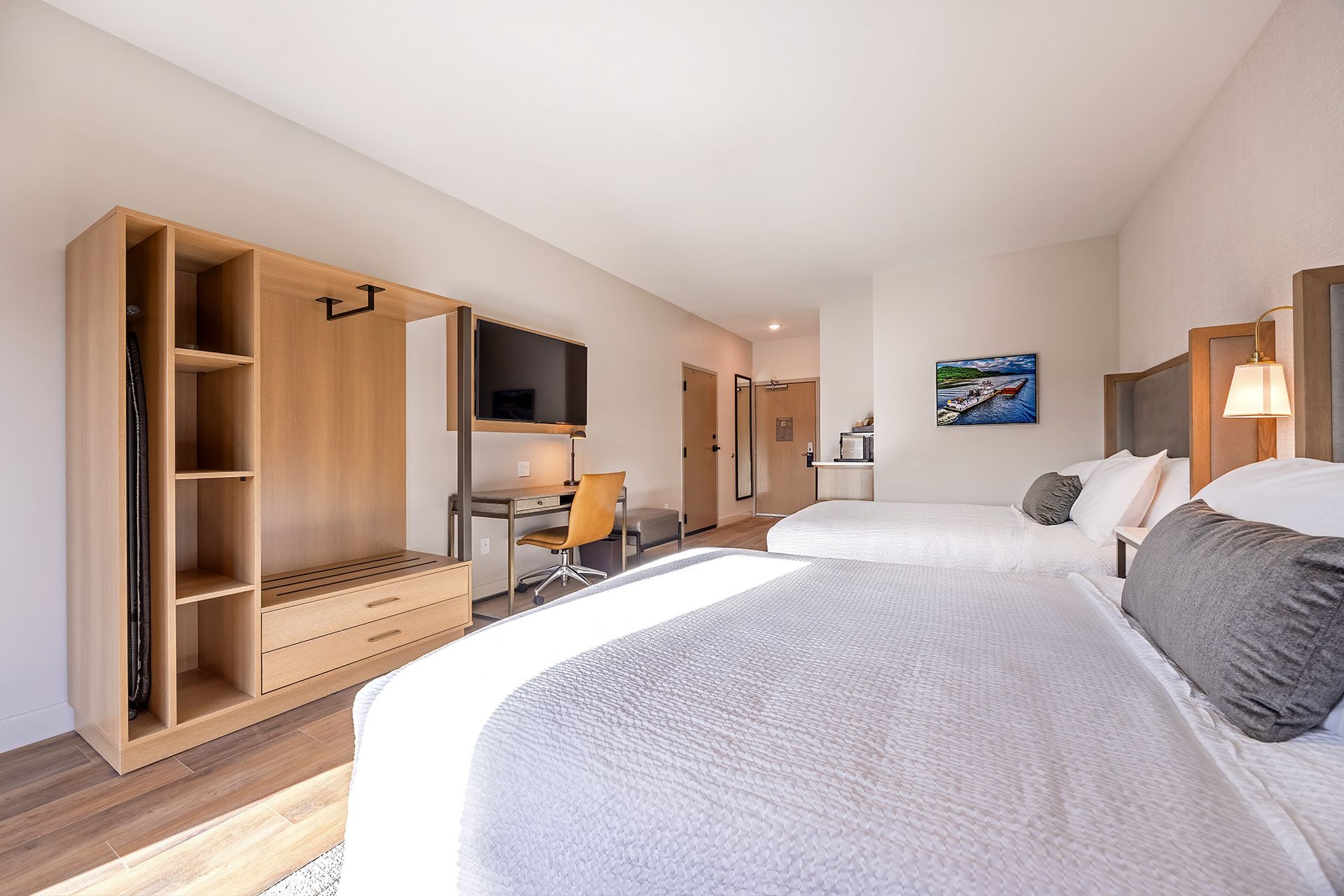 Hotel room with two beds, wooden wardrobe, desk, and TV. Bright, airy, with neutral tones.