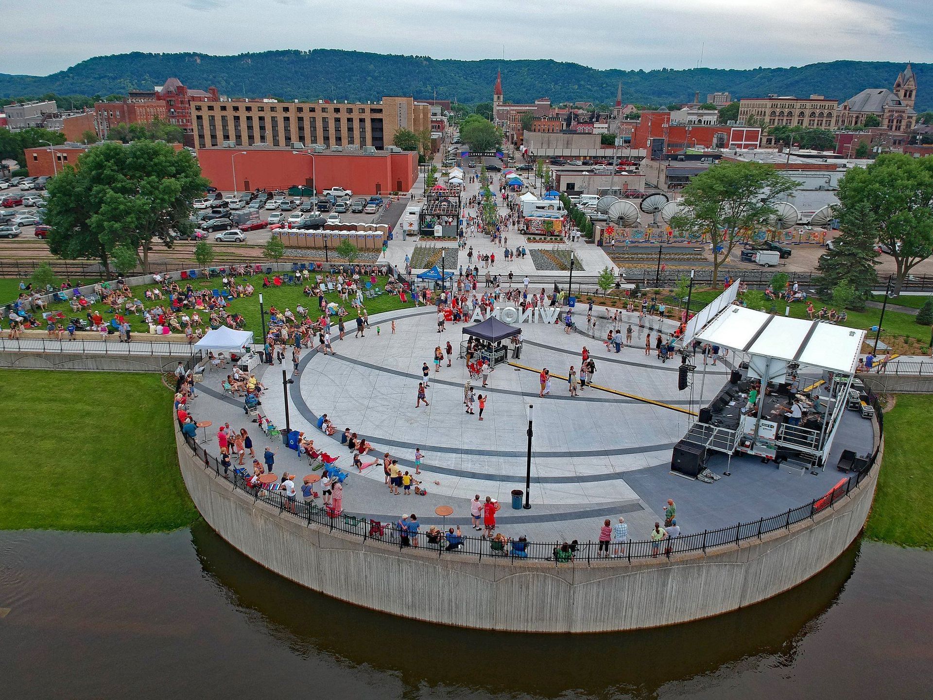 Plate of food with a bun, greens, and sauce, with beer and bowl of nuts on a wooden table.