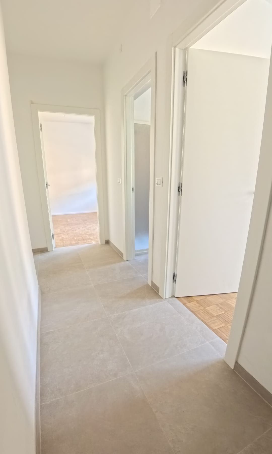 Corridoio con porte aperte, pareti e pavimento chiari, che conduce ad altre stanze.