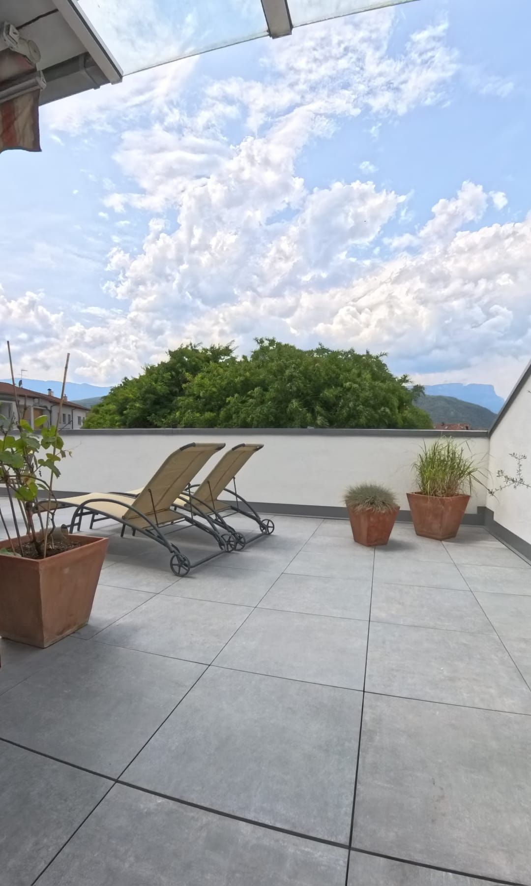Terrazza panoramica con sedie a sdraio, piante in vaso e cielo nuvoloso.