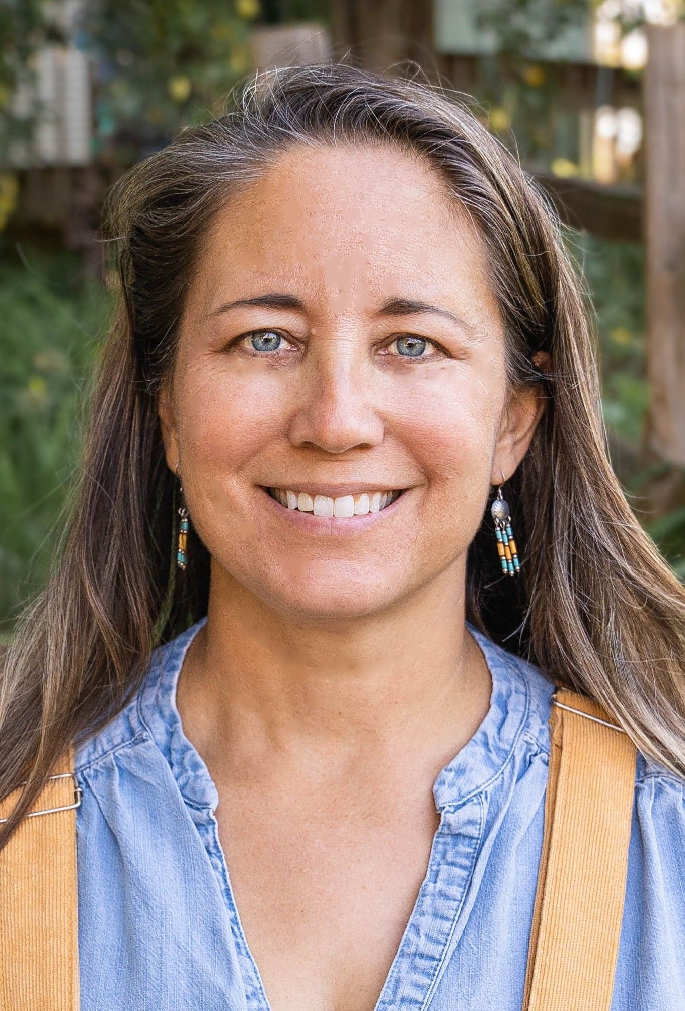 A woman wearing a blue shirt and earrings is smiling for the camera.