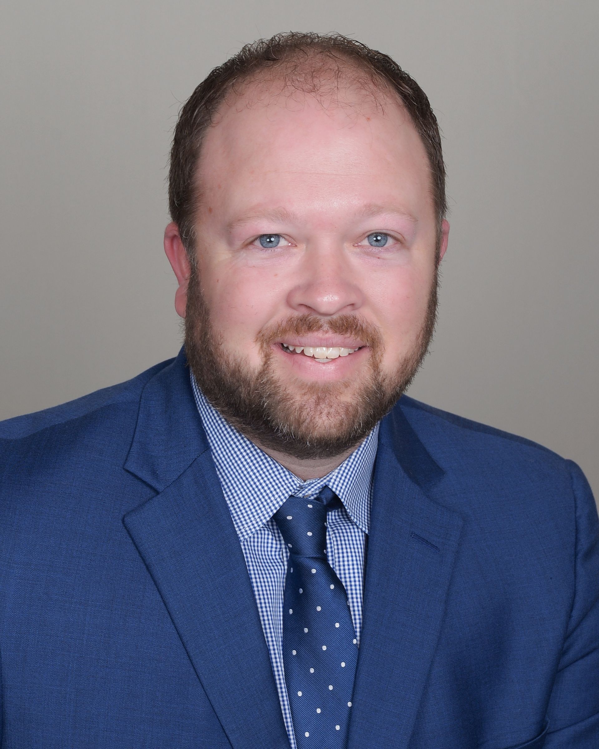 A man with a beard is wearing a blue suit and tie.