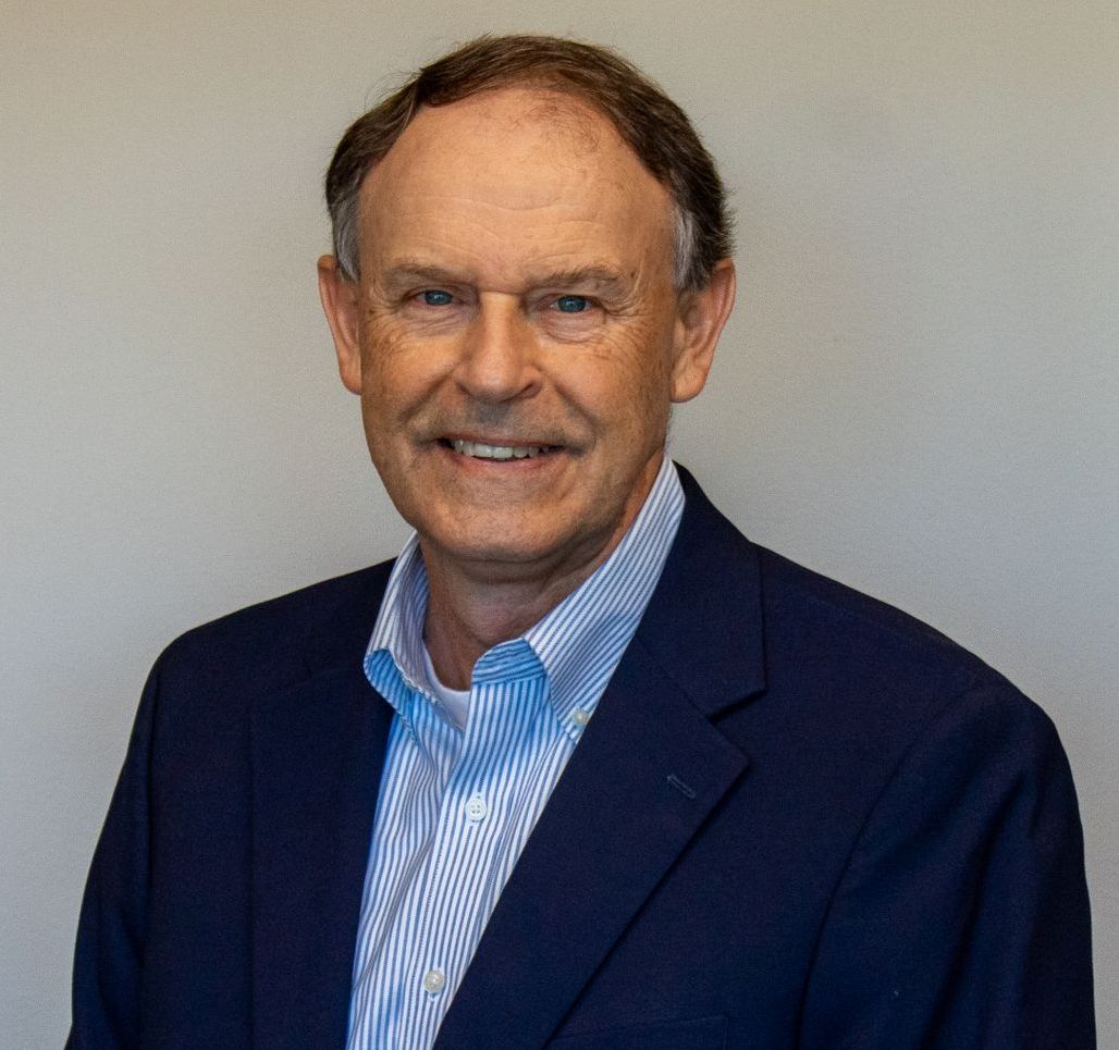 A man wearing a blue jacket and striped shirt is smiling for the camera.