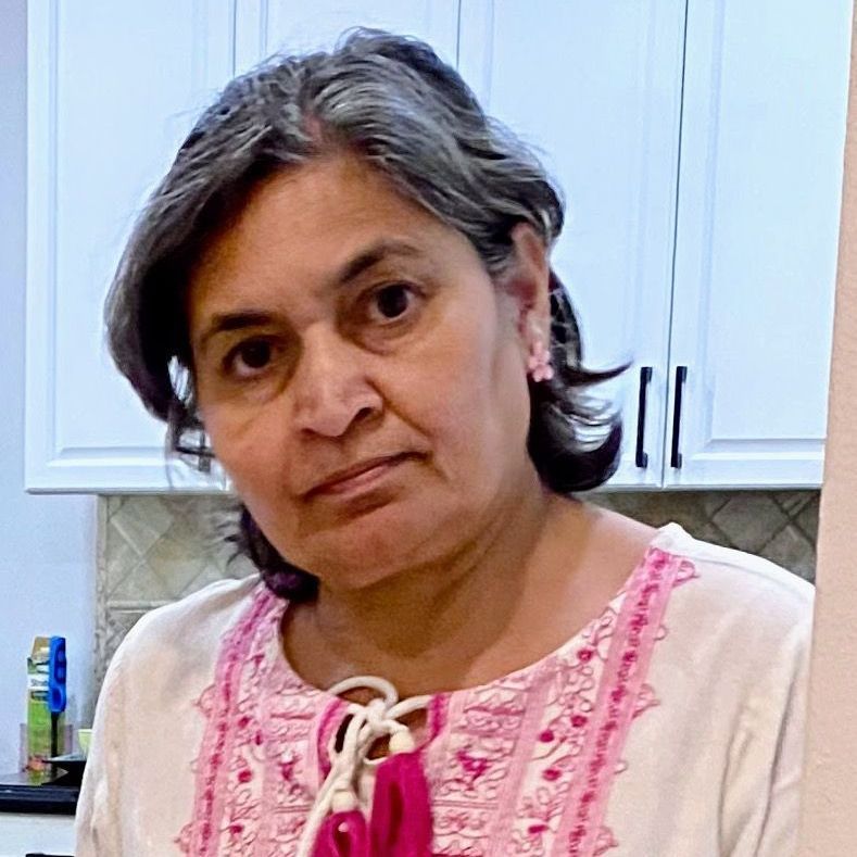 A woman in a pink shirt is standing in a kitchen.