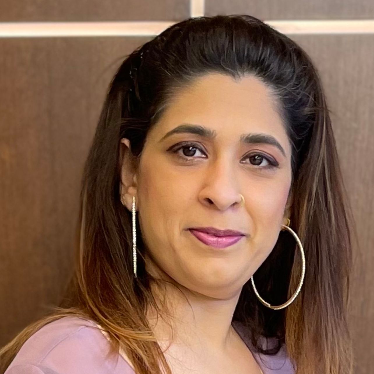 A woman wearing hoop earrings and a nose ring is looking at the camera.