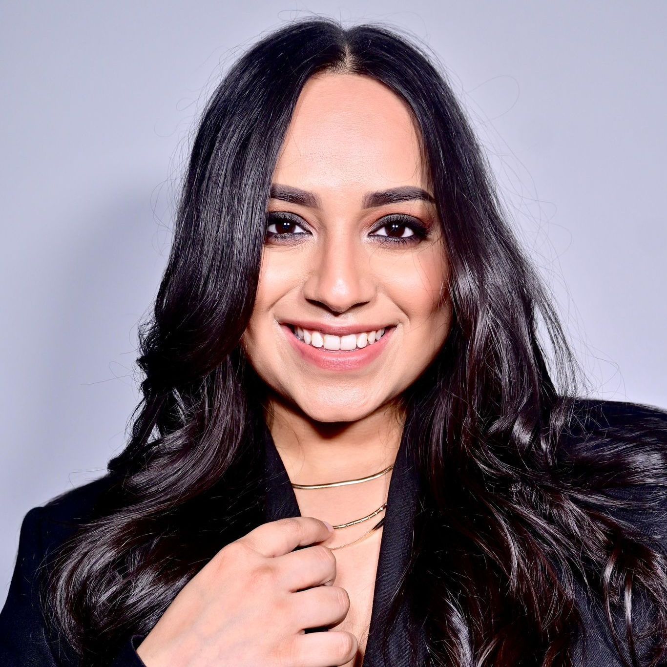 A woman with long dark hair is smiling and wearing a black jacket.