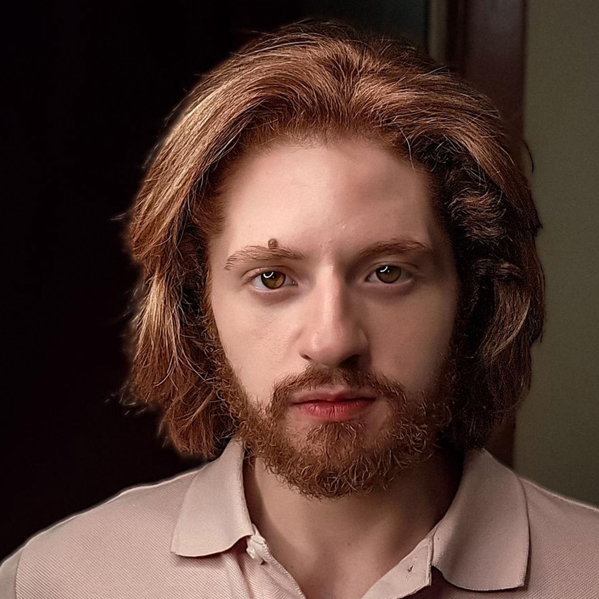 A man with long red hair and a beard is wearing a pink shirt.